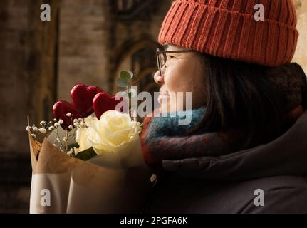 Asian woman holding a bunch of flowers and red hearts for valentines Stock Photo
