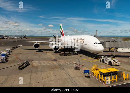 Emirates A380 airliner jet plane A6-EVR on stand at Auckland Airport, New Zealand. Connected to air bridge with tug attached and LSG Sky Chefs loading Stock Photo