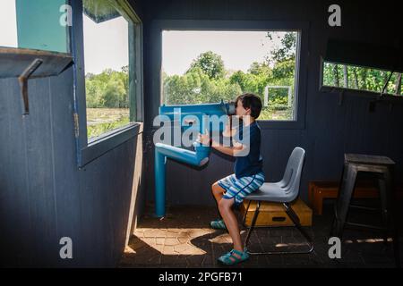 A boy sits by window looking at birds through binoculars Stock Photo