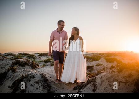 Husband & Pregnant Wife Holding Hands on Beach at Sunset in San Diego Stock Photo