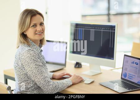 Positive female employee compares statistics on devices Stock Photo