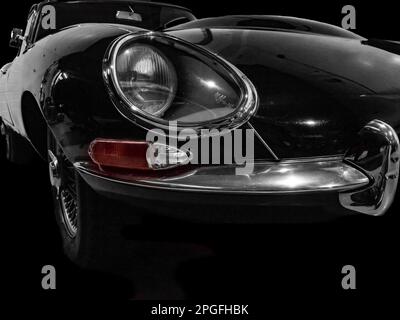 Dramatic close-up of a Jaguar E-Type classic sports car front wing with iconic recessed headlight. Stock Photo