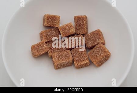 Pile of brown sugar cubes  in a white bowl. Isolated on white background. Stock Photo