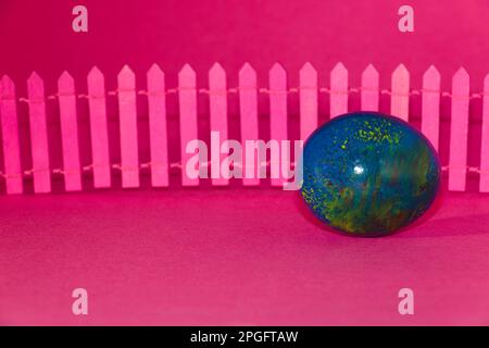 blue colorful egg earth in front of the pink fence on the pink background Stock Photo