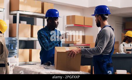 Team of diverse men using scanner and tablet for logistics and inventory, scanning barcodes for merchandise cargo in storage room. Young people in overalls working in stockroom. Stock Photo
