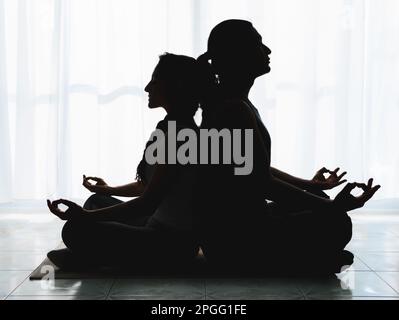Two middle-aged people are doing Yoga indoors, they are in shadows doing deep meditation postures. There is a lot of tranquility in the air. Stock Photo
