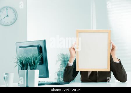 Office workplace, a sign-headed man framed in light wood holds the sign-head with his hands. Either he is very worried or he is pressing his temples w Stock Photo