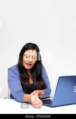 Adult Latina woman suffering from pain, tingling, numbness and weakness in her wrist due to Carpal Tunnel Syndrome while working in her office Stock Photo