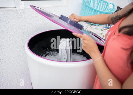 A young Hispanic woman is putting the cover on a top load washing machine Stock Photo