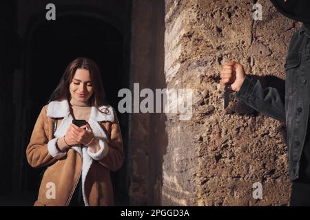 Criminal with knife hiding behind wall and waiting for victim near alley at night Stock Photo