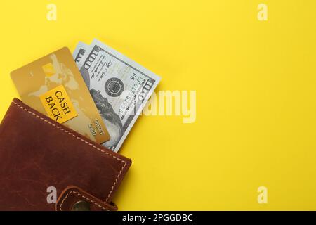 Dollar banknotes and credit card in wallet on yellow background, top view with space for text. Cashback concept Stock Photo