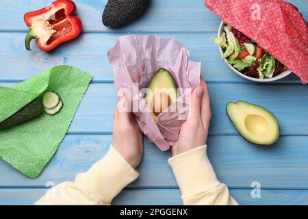 Woman packing half of fresh avocado into beeswax food wrap at light blue wooden table, top view Stock Photo