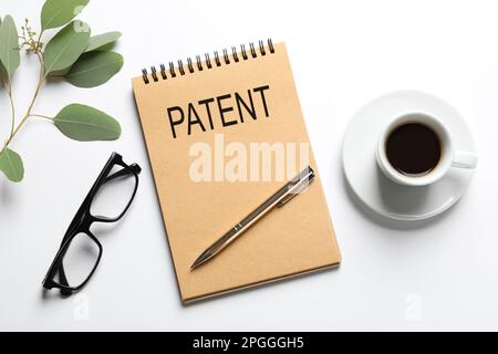 Notebook with word PATENT, pen, cup of coffee, glasses and plant on white table, flat lay Stock Photo