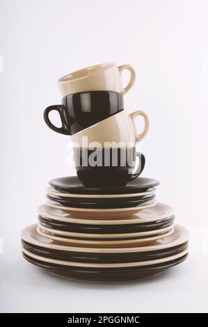 stack of clean dishes in brown and beige - dinner and side plates saucers and cups - mix and match dishware tableware or crockery Stock Photo