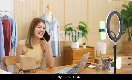 Online merchant concept, Fashion designer holding parcel box and talking on smartphone with client. Stock Photo