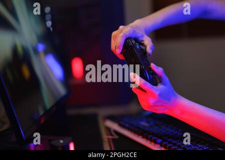 Female cyber hacker gamer use joystick to competition and playing games on computer in neon light. Stock Photo