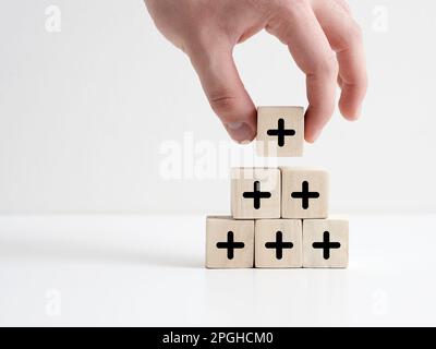 Added value or increasing benefits concept. Progress and profit to benefit growth and development in business. Hand places cube with plus symbol on to Stock Photo