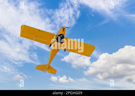 Yellow single-engine ultralight airplane flying in the blue sky with white clouds Stock Photo
