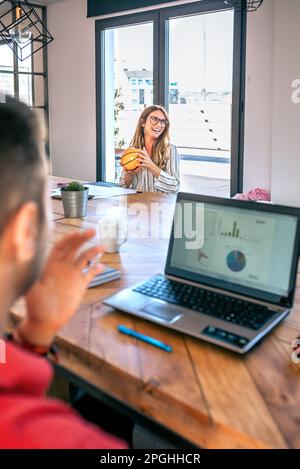 Smiling businesswoman holding small basket ball and having fun playing with colleagues in office Stock Photo