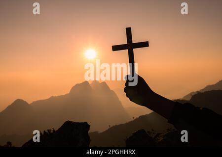 Silhouette off hands holding wooden cross  on sunrise background, Crucifix, Symbol of Faith. Stock Photo