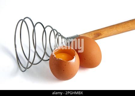 Two beige chicken eggs and a rare eggbeater for beating. Ingredients for cooking isolated on white background Stock Photo