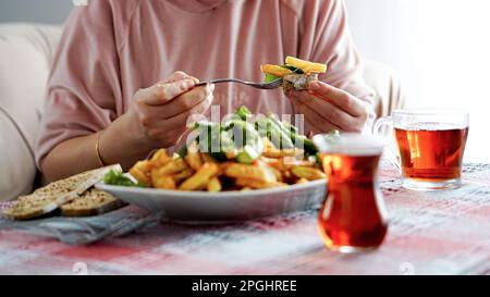 Woman having breakfast with fried potatoes, fried green long pepper, bread and turkish tea, traditional turkish breakfast Stock Photo