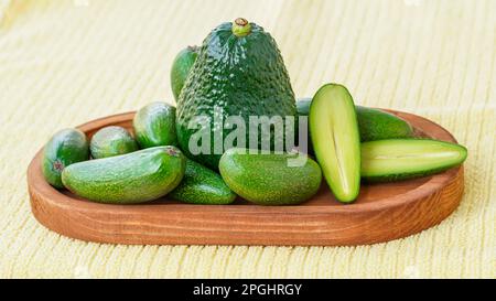 Seedless coctail baby mini avocados whole and half, one avocado in the middle, whole them on the wooden plate, selective focus, closeup Stock Photo