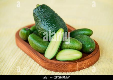 Seedless coctail baby mini avocados whole and half, one avocado in the middle, whole them on the wooden plate, selective focus, closeup Stock Photo