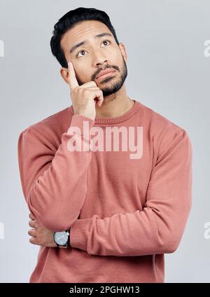Thinking, confused and question with a man in studio on a gray background looking thoughtful or contemplative. Doubt, idea and memory with a young Stock Photo