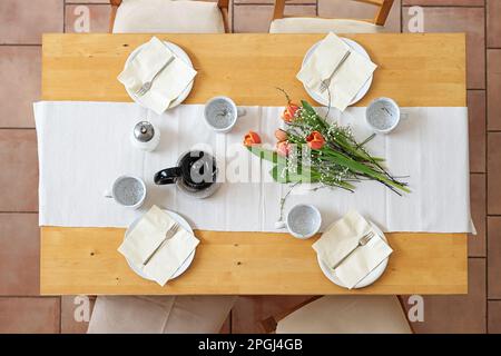 Setting for an afternoon coffee break with four plates, cups, napkins, coffee pot and tulip flowers on a white table runner on a wooden table, top vie Stock Photo