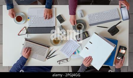 Office desk with hands of for people working together on a joint business project with laptops, papers, calculator and coffee, top view from above, se Stock Photo