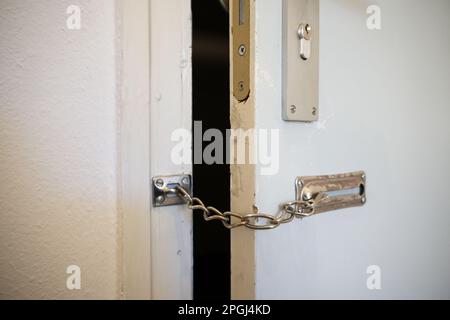 Door chain on an old flat door, hooked in against unwanted visitors and thieves, security and safety at home concept, copy space, selected focus, narr Stock Photo