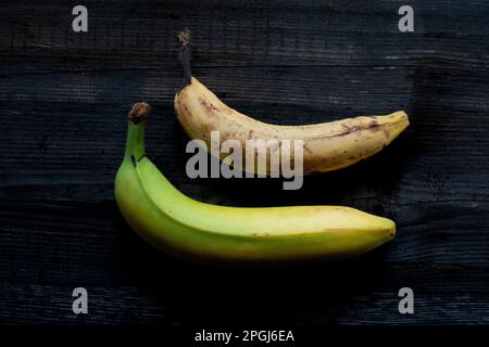 A ripe yellow banana resting on a brown banana against a rustic wooden background Stock Photo