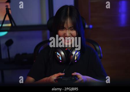 Female cyber hacker gamer using controller joystick to playing games on computer with serious face. Stock Photo