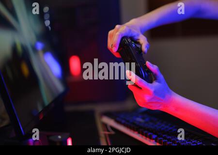 Female cyber hacker gamer use joystick to competition and playing games on computer in neon light. Stock Photo