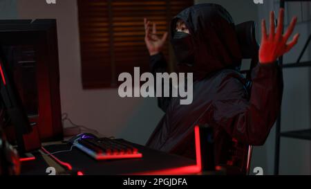 Hacker in hoodie raising hands while having problem with hacking programming system or server. Stock Photo