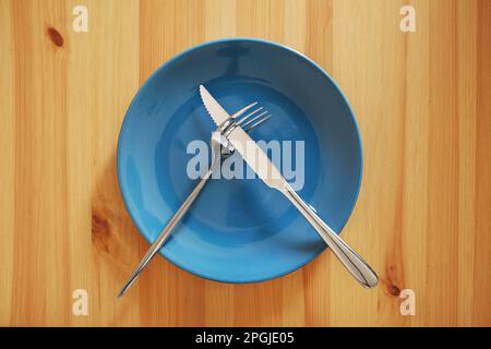 Empty and clean blue plate with fork and knife on a wooden table Stock Photo
