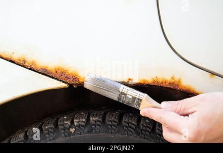 Close up view of person hand apply home use car rust stop liquid on vehicle rusty parts. Stock Photo