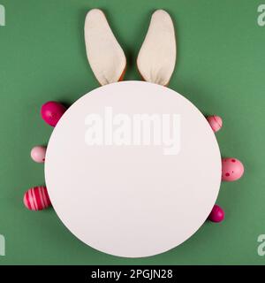 Bunny ears, white circle and Easter eggs on green background Stock Photo