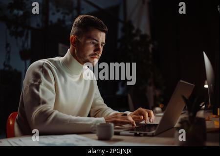 Focused man using laptop for work and trying hurry up to deadline while sitting in the modern office Stock Photo