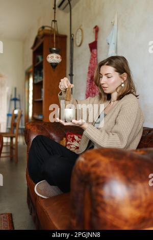 Young woman playing on a singing tibetian bowl.Relaxation and meditation.Sound therapy,alternative medicine.Buddhist healing practices.Clearing space of negative energy.Selective focus,close up.  Stock Photo