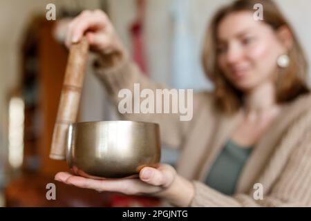 Young woman playing on a singing tibetian bowl.Relaxation and meditation.Sound therapy,alternative medicine.Buddhist healing practices.Clearing space of negative energy.Selective focus,close up.  Stock Photo