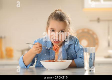 Cute little girl eating tasty pasta at table in kitchen Stock Photo