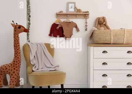 Wooden shelf with baby clothes, toys and furniture in room. Interior design Stock Photo