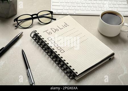 Notepad with unfilled To Do list, pens, glasses and cup of coffee light on grey marble table Stock Photo