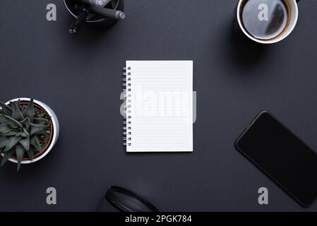 Blank notepad on black desk surrounded by coffee mug, phone, plant, pens and camera lens. Concept business flat lay composition Stock Photo