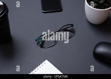 Glasses on black office desk surrounded by office supplies. Modern business composition Stock Photo