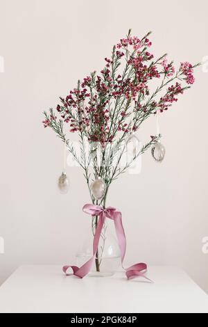 Easter eggs hang on a sprig of flowers in a transparent vase. Stock Photo