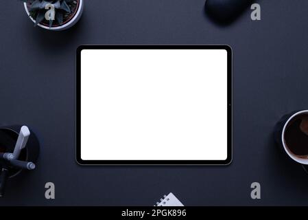 Tablet mockup on black desk with plant, pens, coffee mug, glasses box, and pad,. Top view, flat lay composition Stock Photo