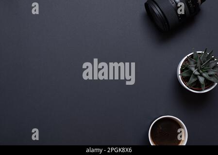 Photographer work desk composition with camera lens, plant and coffe mug. Top view, flat lay with copy space on black desk Stock Photo